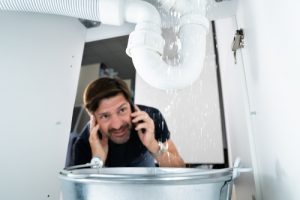 Worried,man,calling,plumber,while,watching,water,leaking,from,sink